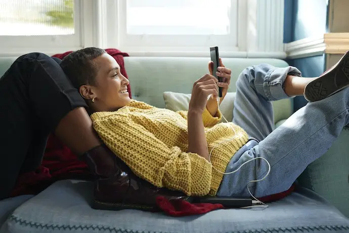 mulher deitada no sofá com celular na mão enquanto carrega com cabo grande
